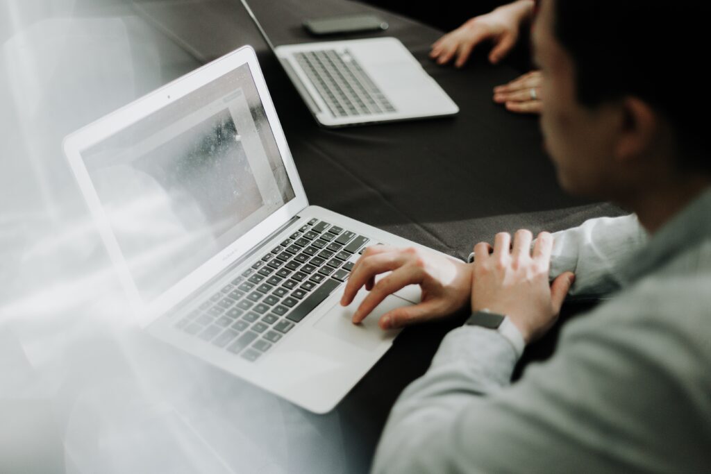 Person using their laptop mouse sitting next to someone who is also looking at a laptop