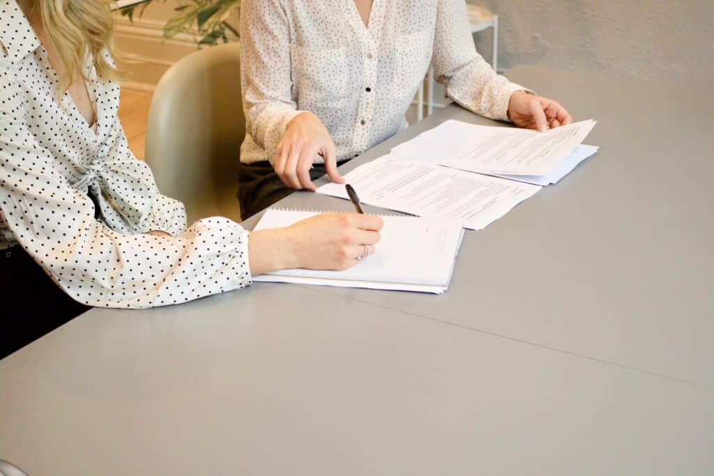 Two women from the neck down sitting together while one fills out paperwork