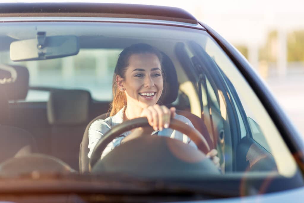 A happy young driver behind the wheel of her car. The best auto insurance companies of 2025 offer affordable coverage options for safe and new drivers.