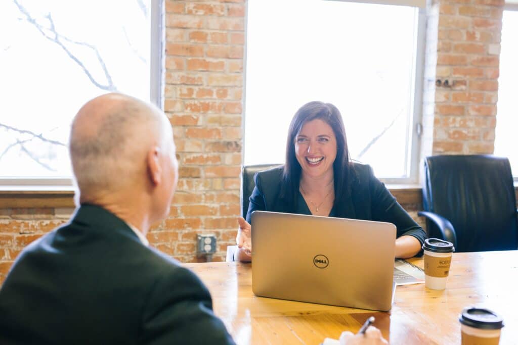 A woman with a Dell laptop meeting with a man at a wooden table in a brick office