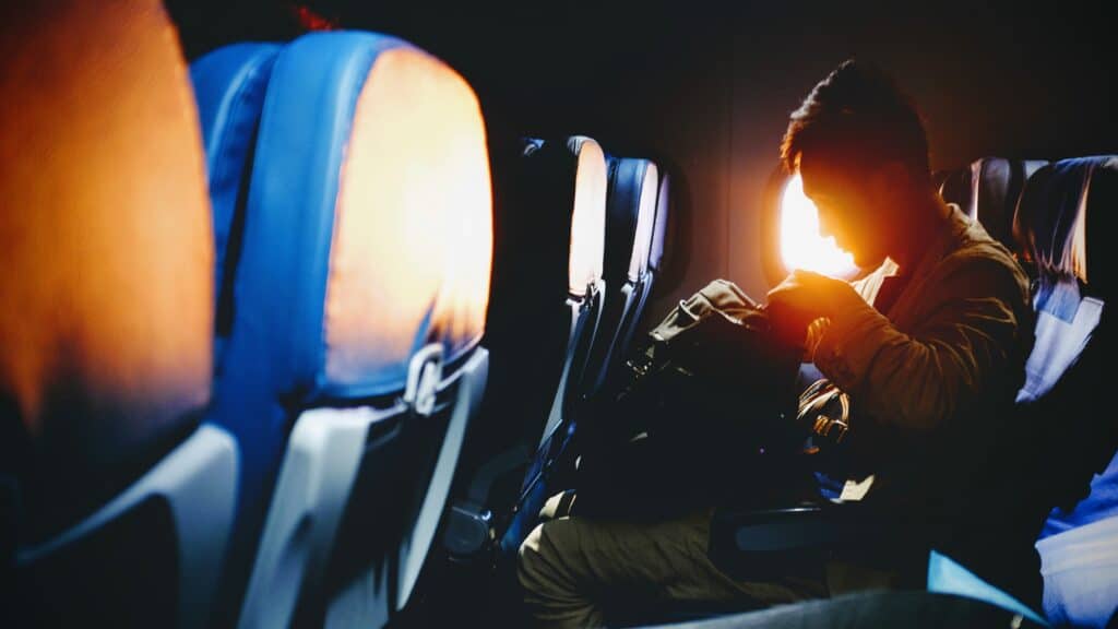 Person sitting on a plane during sunset looking through their backpack on their lap