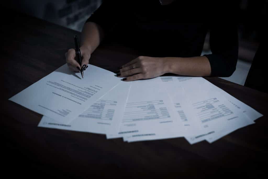 A person's hands filling out various sheets of paper with a pen