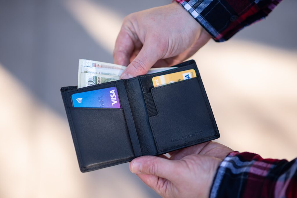 Hands pulling out money of a black wallet with two Visa cards showing