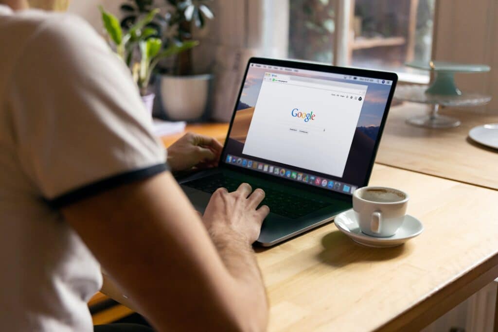 Person pulling up Google on their laptop while drinking a cup of coffee