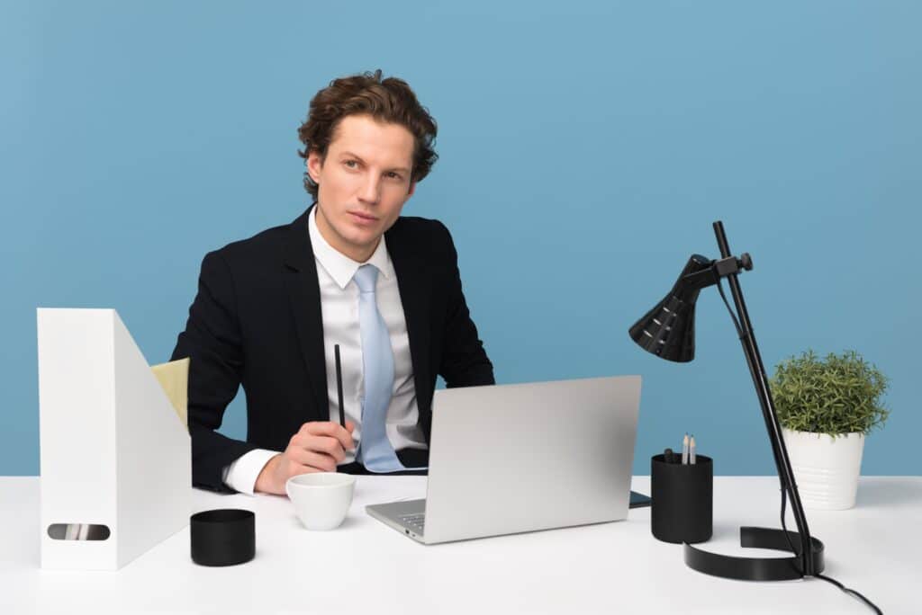 Man in a suit sitting at a desk in front of a bright blue wall