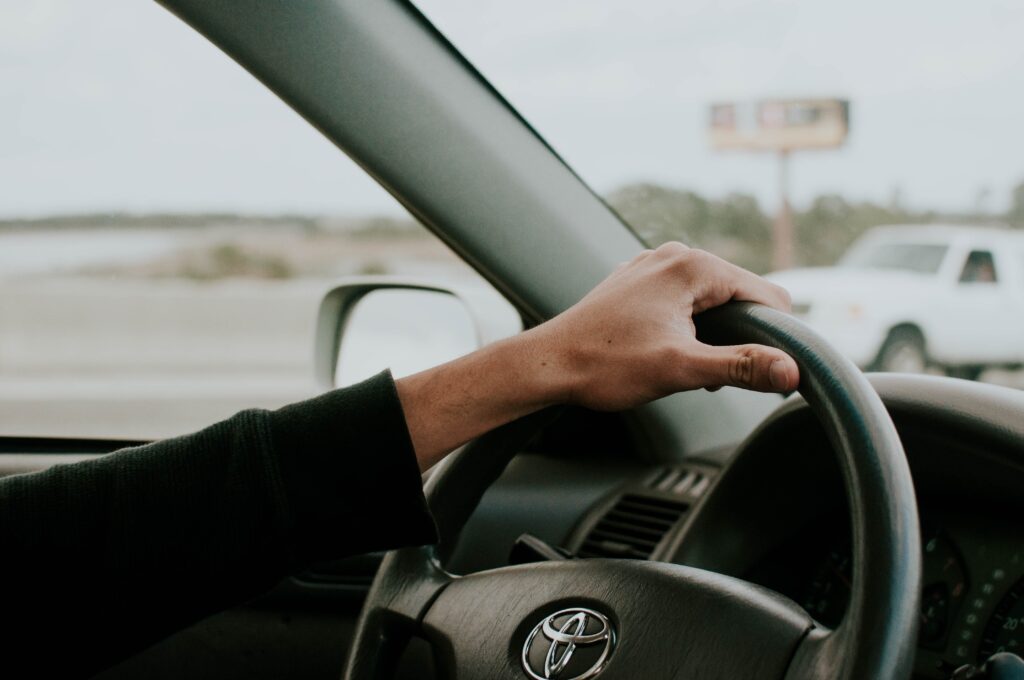 One hand on the steering wheel driving a Toyota