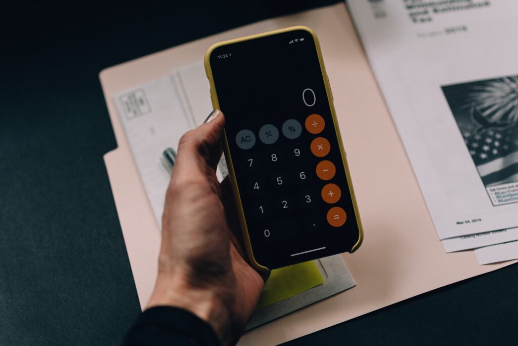 A person's hands holding their phone open to the calculator app at 0 over a folder of papers