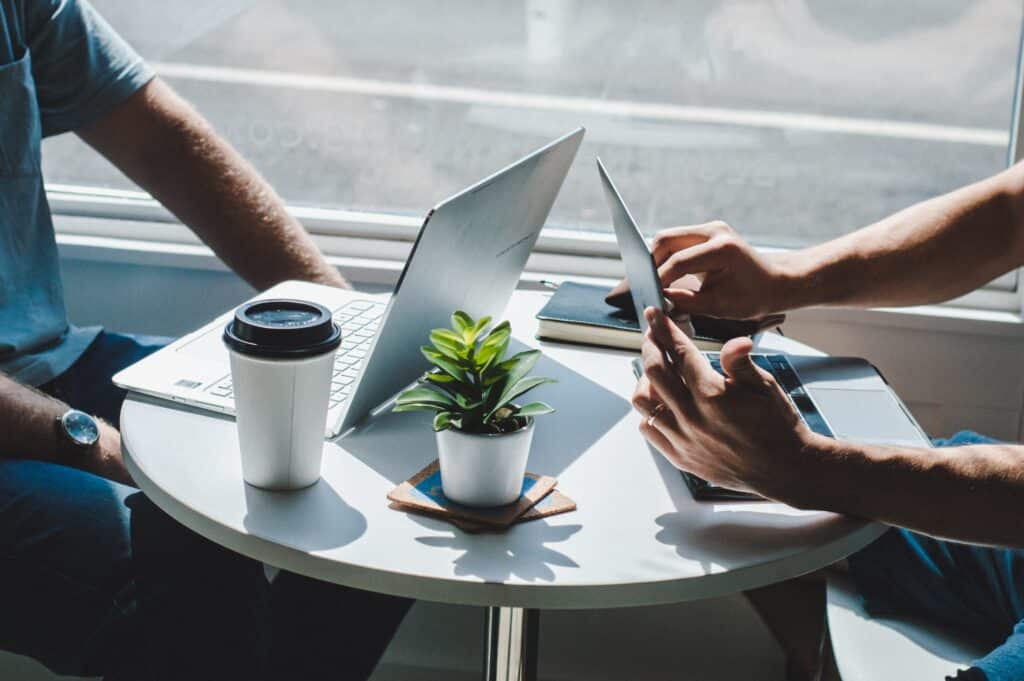 Two people from the arms down sitting at a round table with their laptops