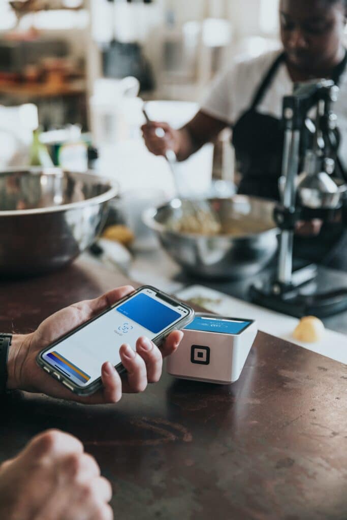 Person holding Apple Pay up to a card reader while another person mixes batter in a bowl