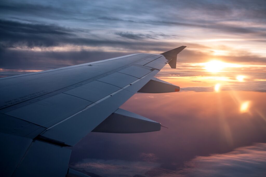 One wing of an airplane flying through the sky at sunset