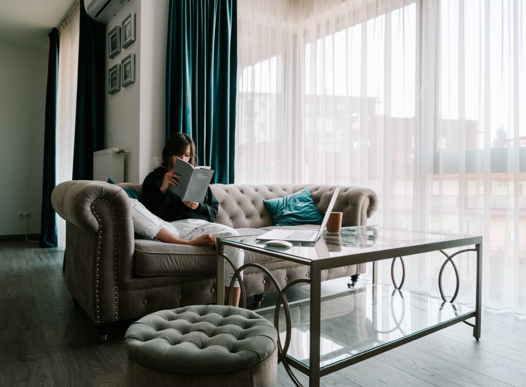 Woman sitting on a tan couch in a living room reading a manual or guide