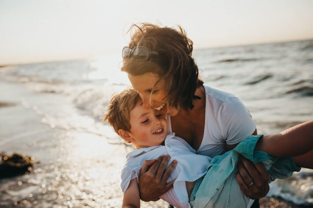 Woman smiling and holding a toddler boy in the ocean