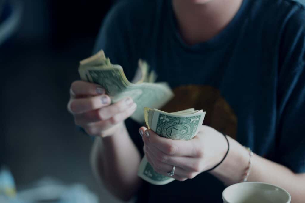 A person's hands as they count through a stack of dollar bills