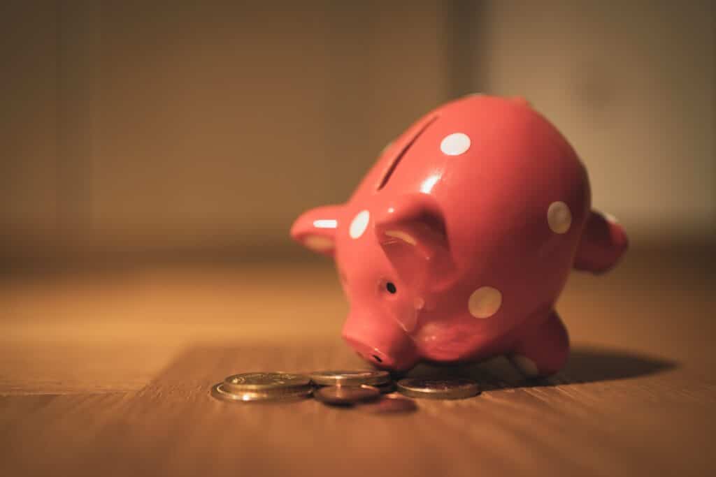 Tipped over pink and white polka dot piggy bank leaning over coins