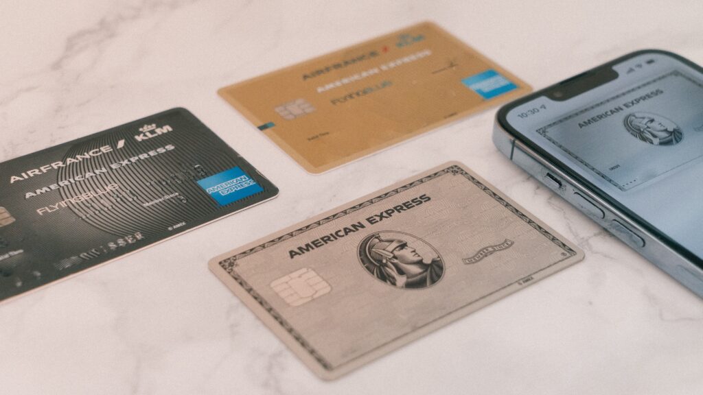 3 American Express cards laying next to a cell phone displaying another American Express card