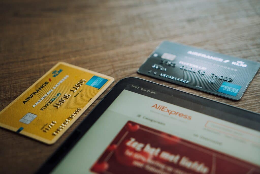 Two American Express cards laying on a table next to a tablet open to AliExpress site