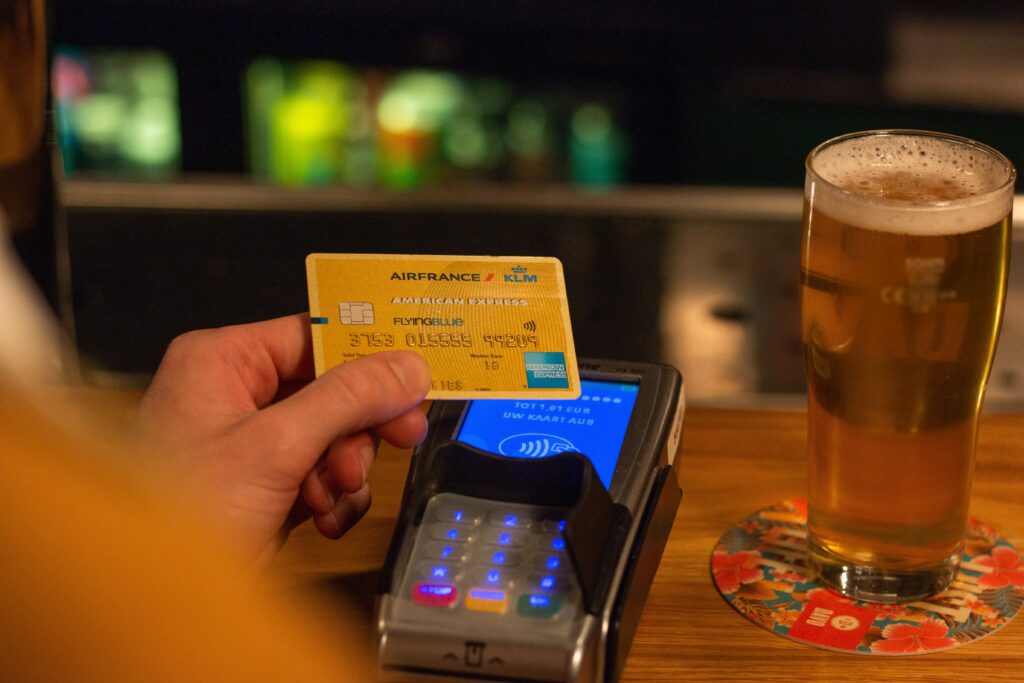 Person holding AirFrance American Express card up to a card reader at a bar