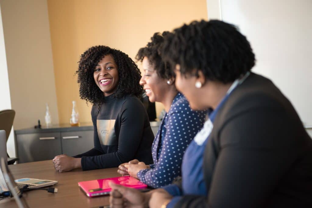 3 women smiling and sitting in a row at a long table in an office setting