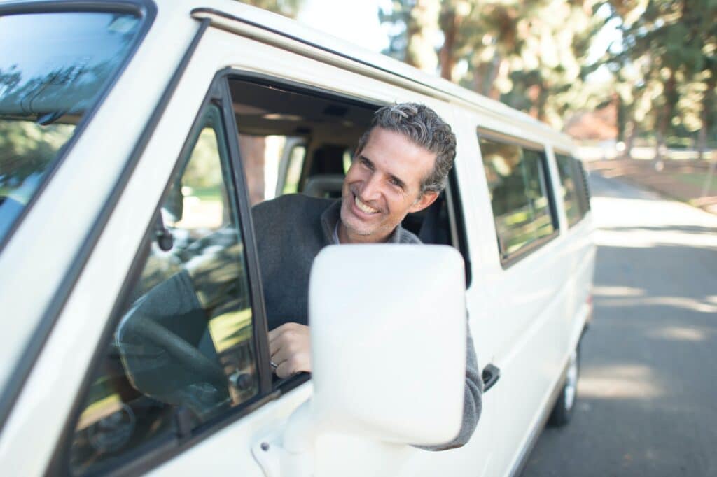 Man smiling with his head out the window driving a white van