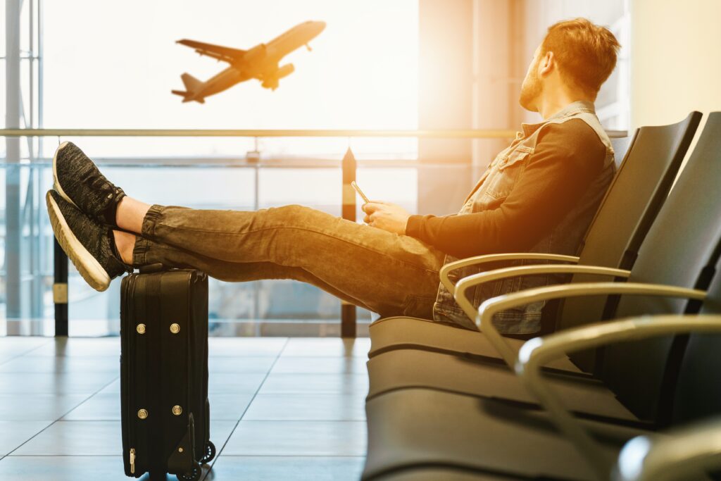 Person sitting in the airport resting their feet on their luggage as they watch a plane takeoff