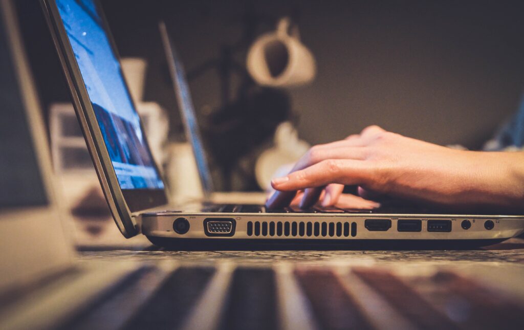 A person's hands from the side typing on a laptop