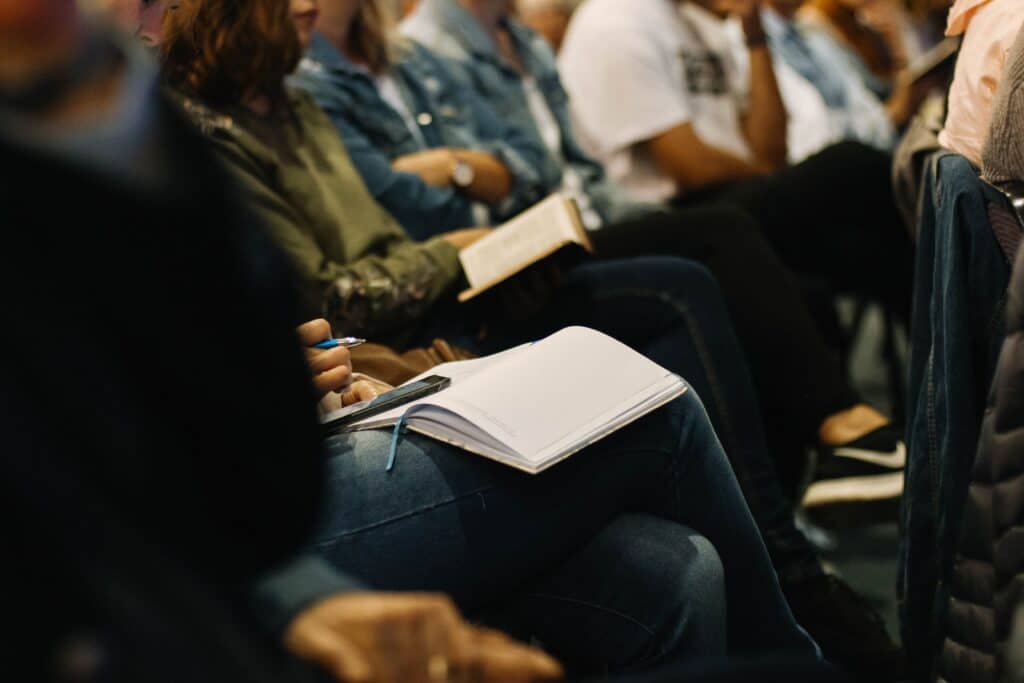 Zoomed in photo of a students lap with a notebook and phone sitting in an auditorium type setting