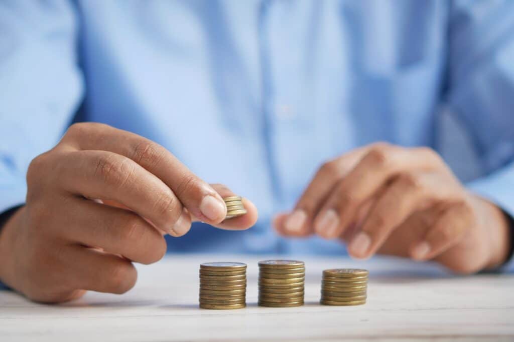 Hands of a person in a button down stacking gold coins into 3 piles