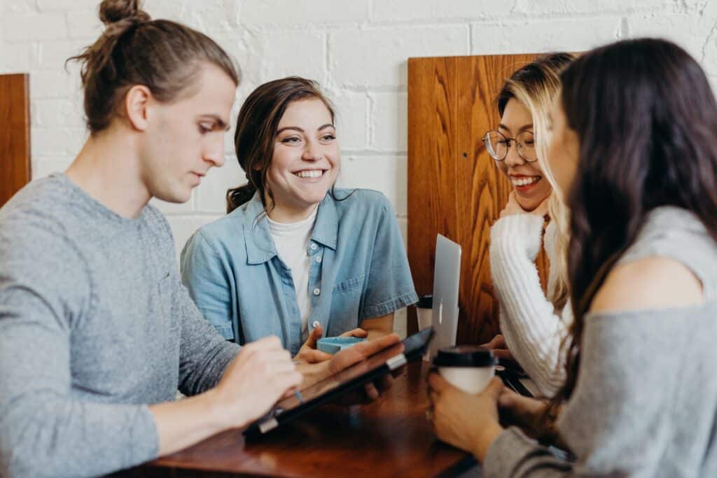 Group of 4 young adults talking over a tablet drinking coffee