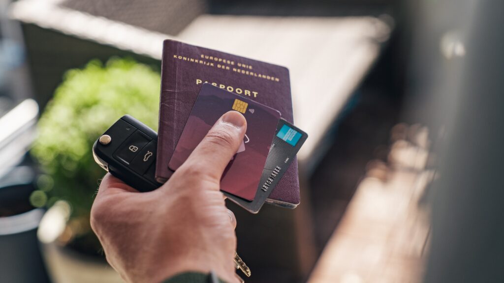 Hands holding a passport, keys and two credit cards