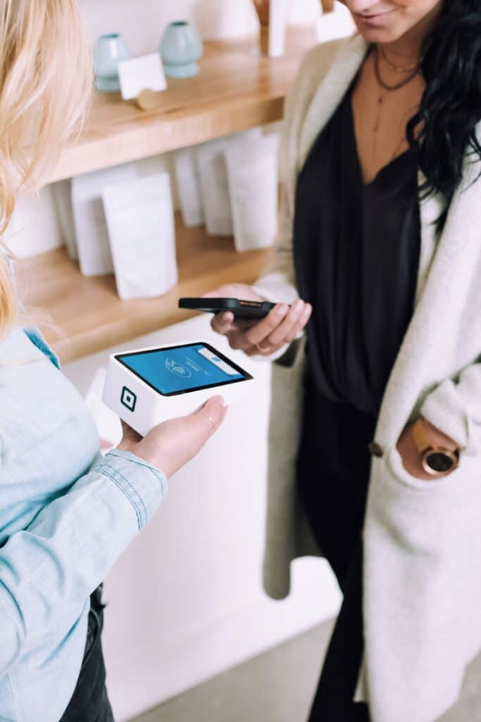 Woman holding her phone in front of a card reader held by another woman