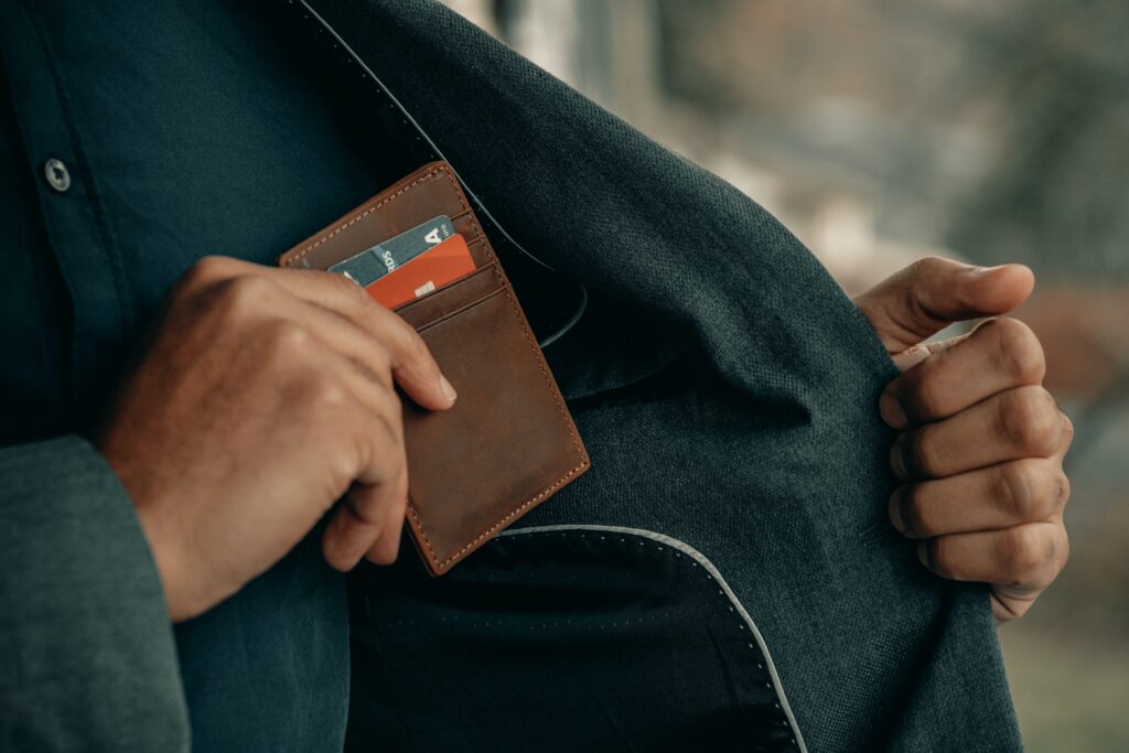 Person putting brown wallet into the inside pocket of their jacket