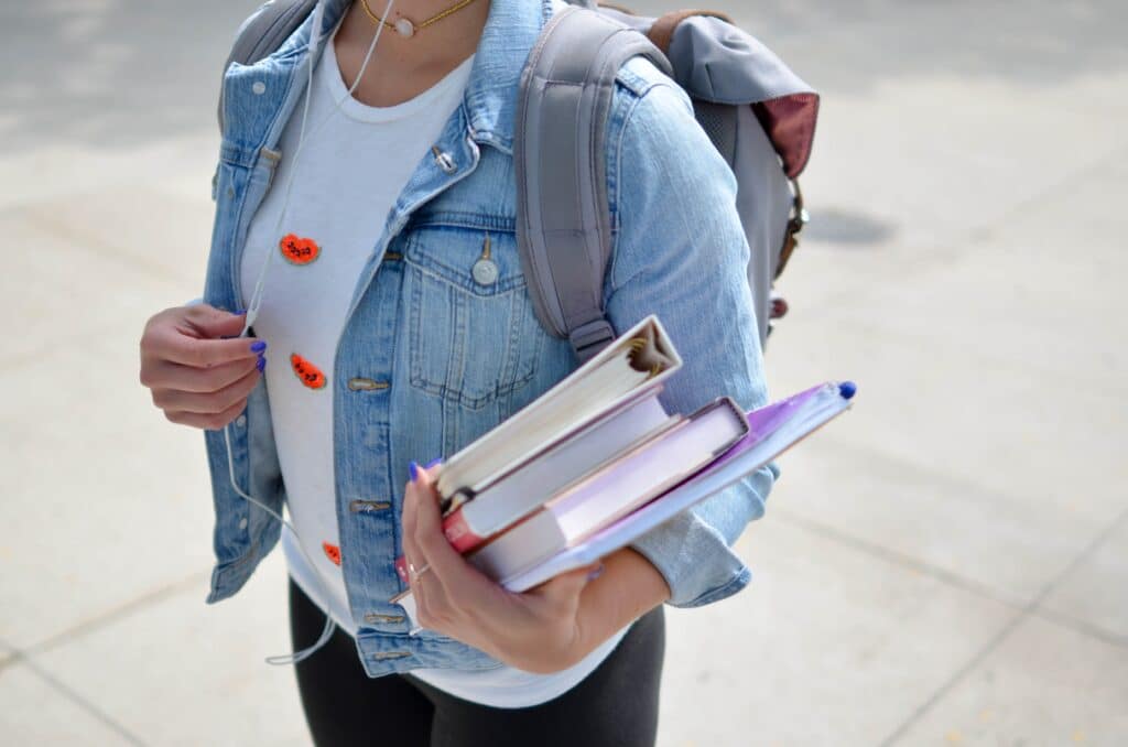 A college student carrying textbooks and wearing a backpack, preparing for classes. Many students rely on student loans and FAFSA to afford higher education.