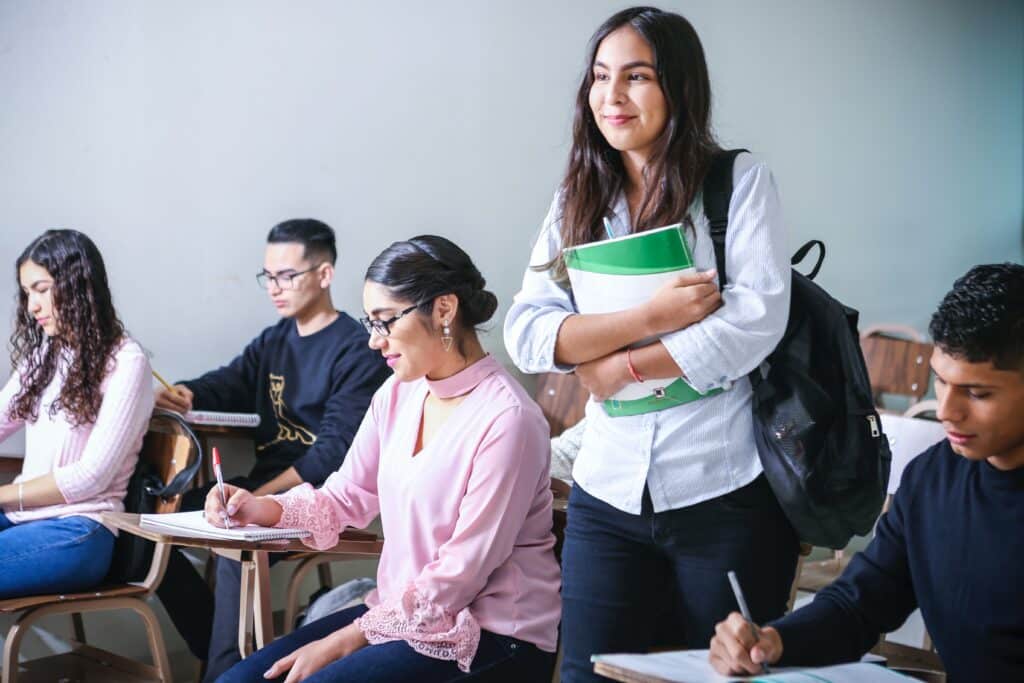 Classroom full of students, most sitting and one standing with backpack