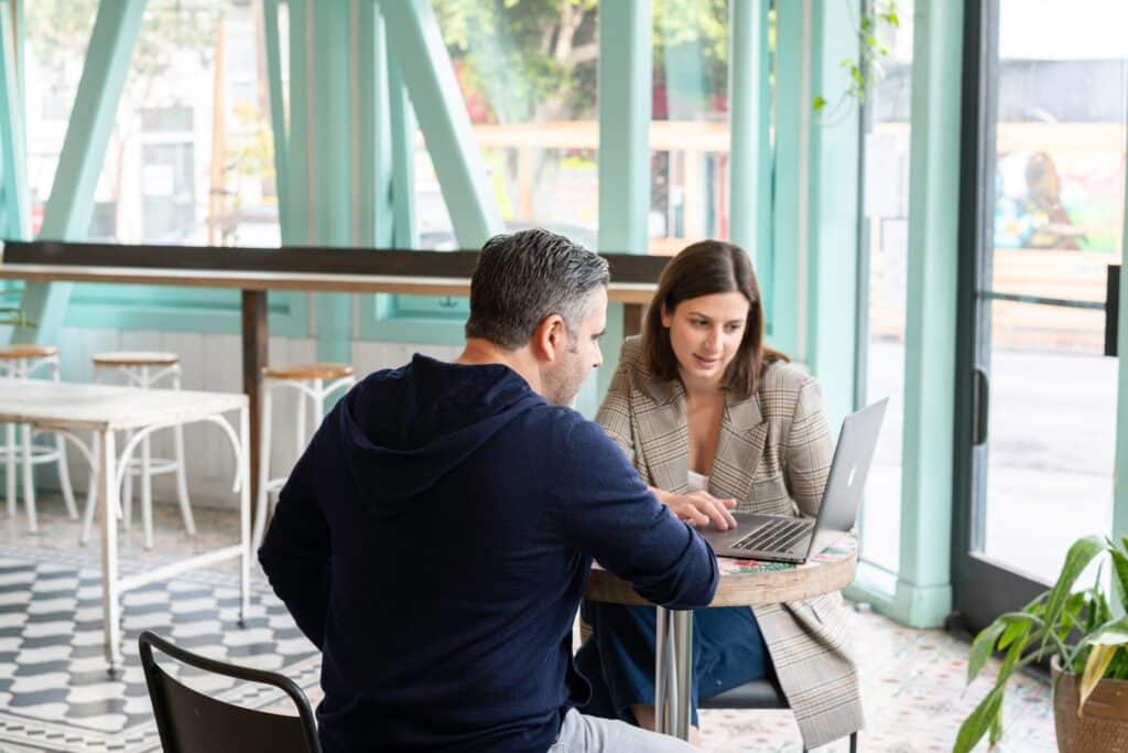 Man and woman sitting around an Apple laptop at a small round table