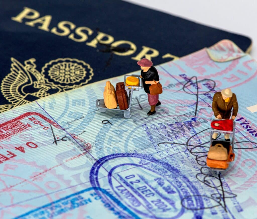 Small figurines with suitcases on top of a stamped passport