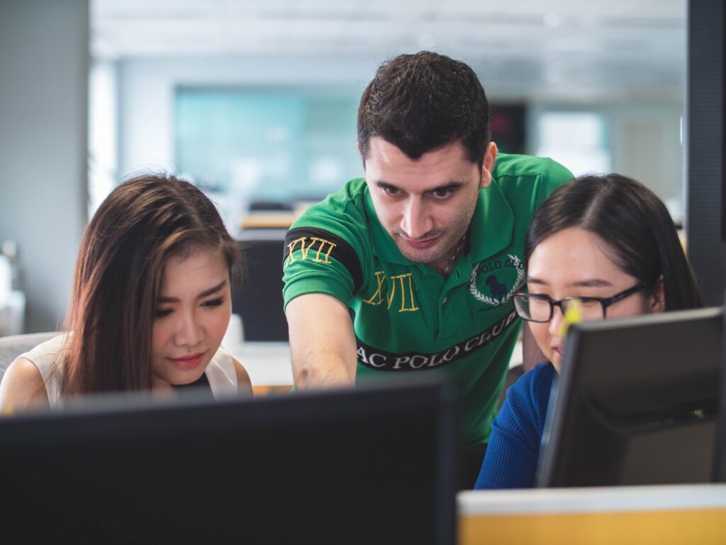 Man helping two students sitting at computers