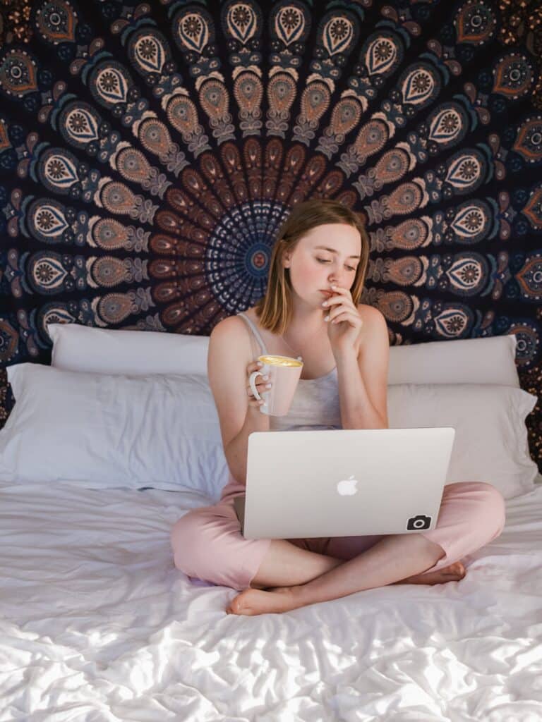 Girl on bed drinking coffee with laptop open