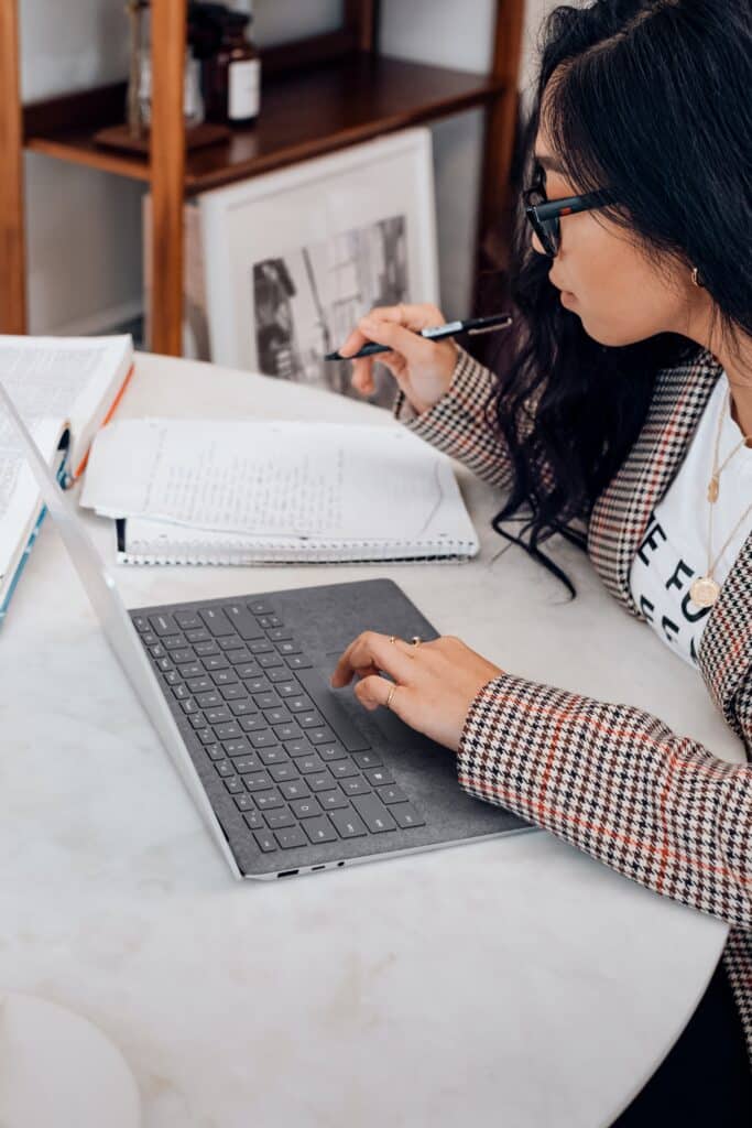 Woman working on her laptop and also taking notes in a notebook