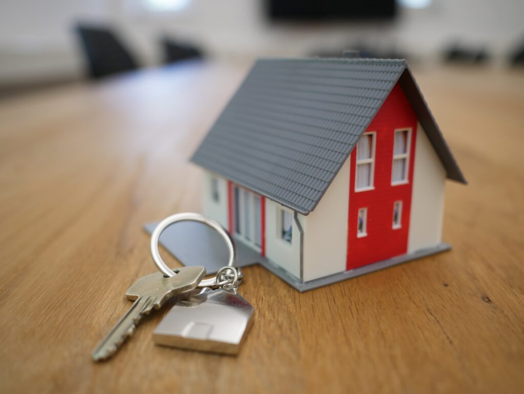 House keys sitting next to a small scale 3 dimensional house model on a wood table