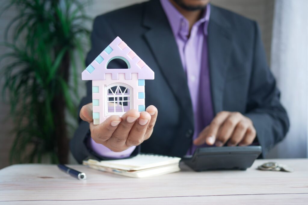 Man in a suit holding a small colorful model house