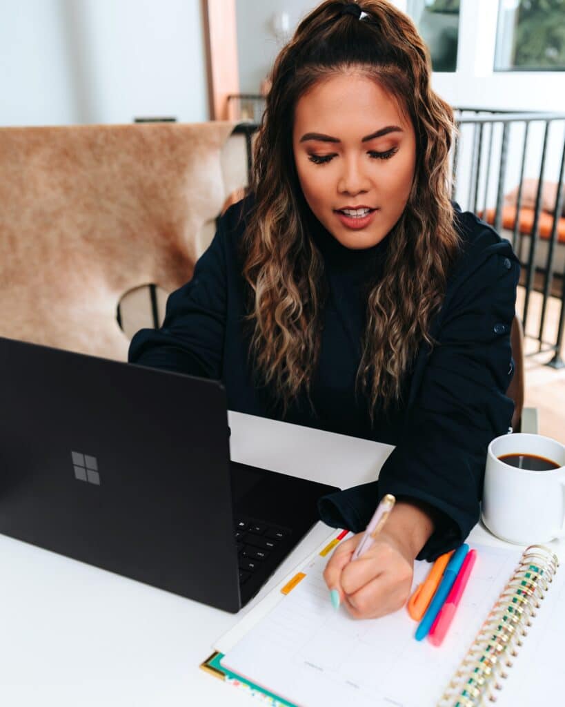 Woman working on her Windows laptop and writing in her planner