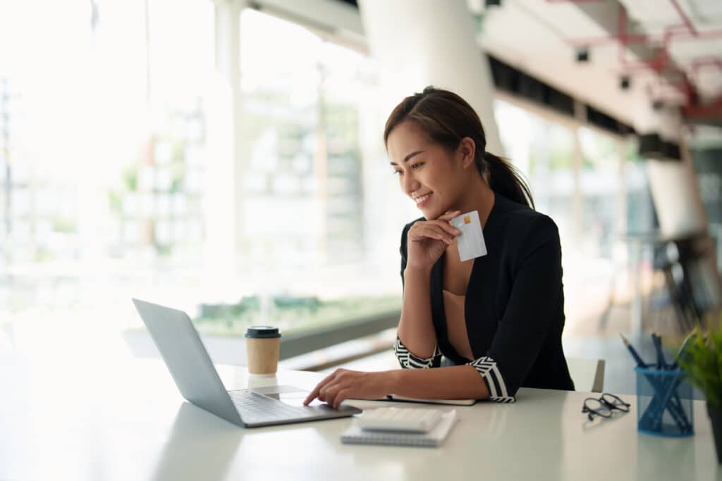 A woman working on her computer holding a credit card.