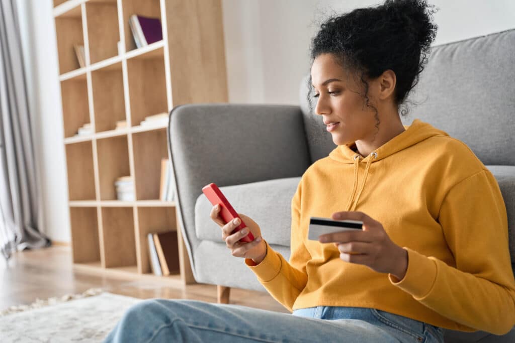 A woman holds her credit card as she uses a smart phone.