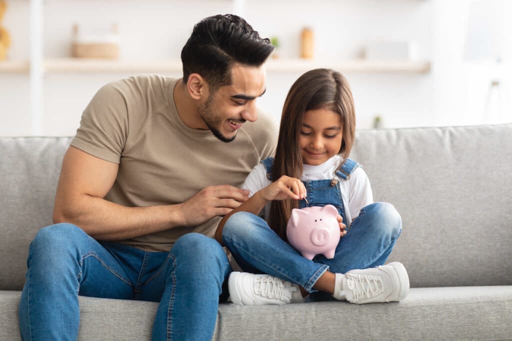 A dad and daughter put money into a piggy bank.