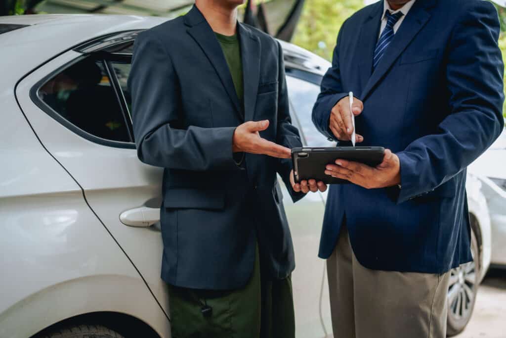 Clients engage with a car insurance agent beside a wrecked vehicle. They examine the policy details, assess the damage, and finalize paperwork related to the insurance claim and repairs.