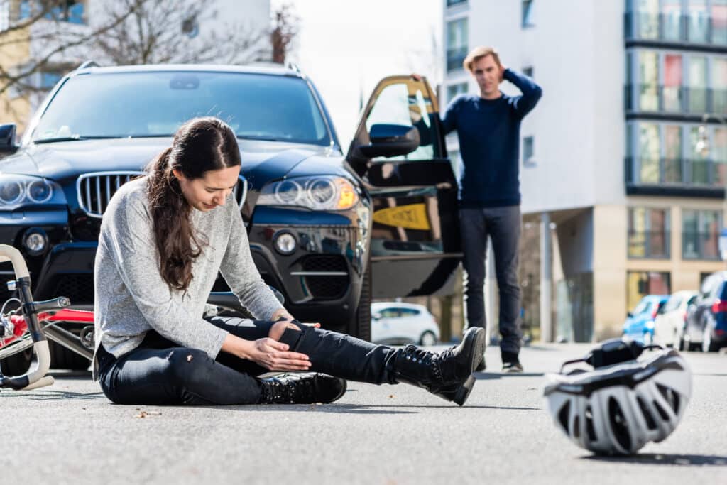 A woman sits on the road holding her injured leg after a car accident involving a cyclist. A personal injury lawyer can help accident victims seek compensation.