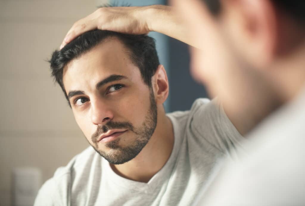 A man examining his hairline in the mirror, concerned about hair loss. Many people explore hair loss treatment options to restore hair growth and scalp health.