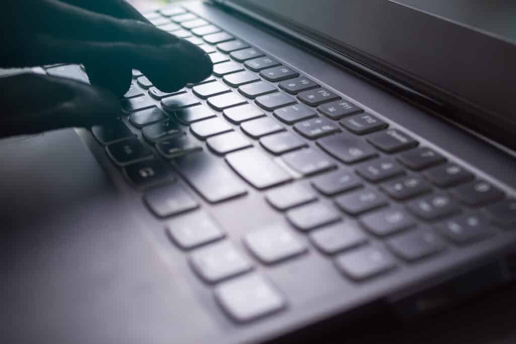 A gloved hand typing on a laptop keyboard, symbolizing cybercrime. Understanding identity theft prevention and recognizing the warning signs of identity theft can help protect personal and financial information.