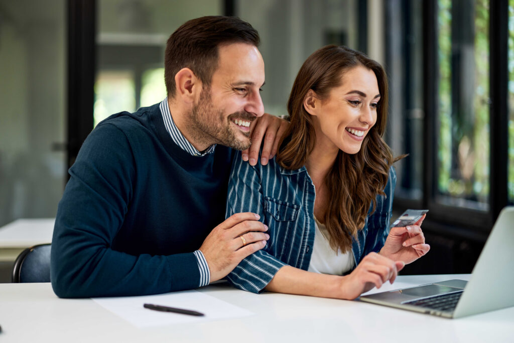 A happy couple reviews checking account options on their computer.